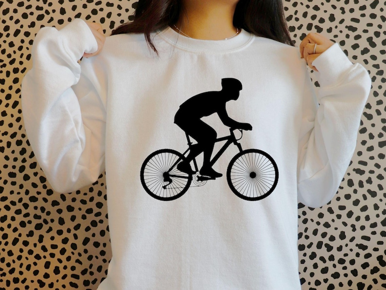 K&ouml;nnte beinhalten: Wei&szlig;es Sweatshirt mit einer schwarzen Silhouette einer Person auf einem Fahrrad.