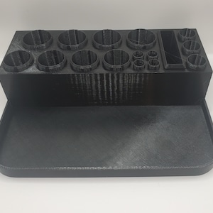May include: A black, 3D-printed organiser with multiple circular compartments of varying sizes, a rectangular slot, and a pull-out tray. The organiser is designed to hold various small items, such as craft supplies or tools.