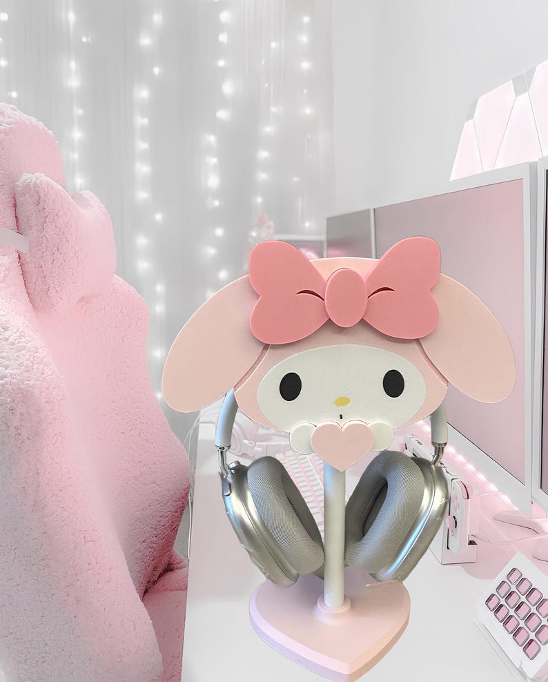May include: Pink Hello Kitty themed headphone stand with a heart-shaped base. The stand is made of wood and features a cute Hello Kitty face with a pink bow.