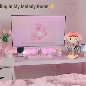 May include: A pink and white themed desk setup with a computer monitor displaying a cartoon character, a keyboard, a mouse, a headset stand, and a pink and white headset. The text "Chilling in My Melody Room" is written in the top left corner of the image.