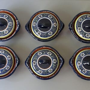 Könnte beinhalten: Sechs blaue und weiße Keramik-Auflaufformen mit Deckeln. Jede Form hat ein Blumenmuster mit weißen Blüten und grünen Blättern. Die Formen haben einen braunen Rand und einen Griff auf jeder Seite.