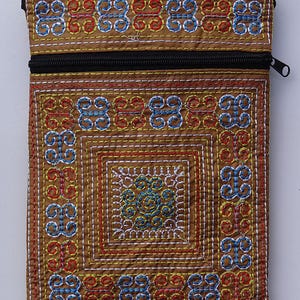 Puede incluir: Una bolsa de tela marr&oacute;n con cremallera negra y patrones bordados intrincados en rojo, azul y amarillo. El dise&ntilde;o presenta formas geom&eacute;tricas y motivos florales, creando un accesorio detallado y colorido.