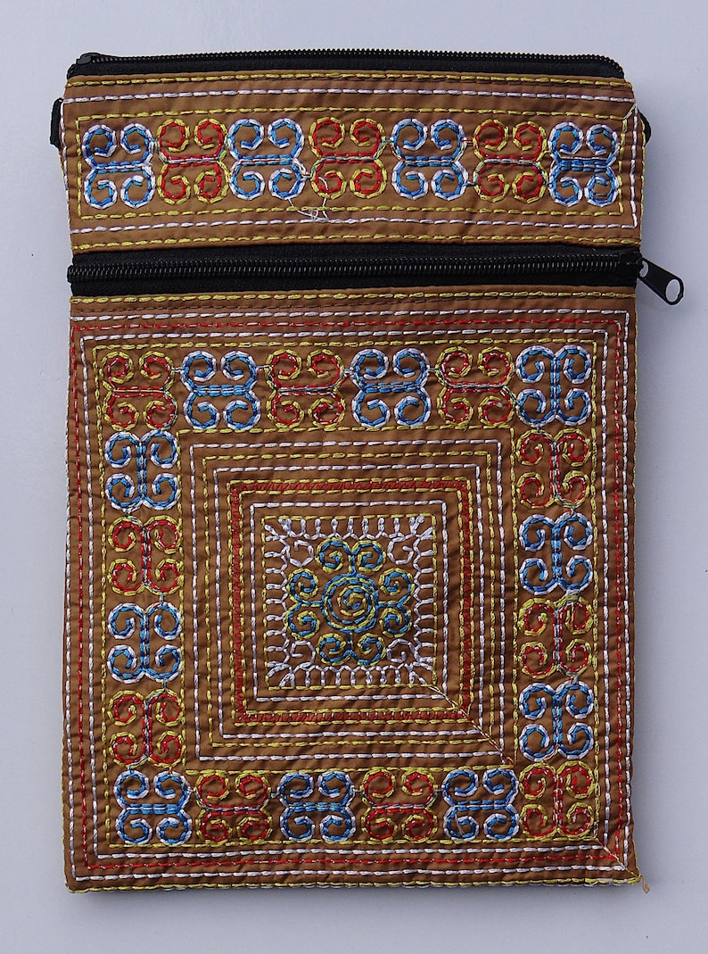 Puede incluir: Una bolsa de tela marr&oacute;n con cremallera negra y patrones bordados intrincados en rojo, azul y amarillo. El dise&ntilde;o presenta formas geom&eacute;tricas y motivos florales, creando un accesorio detallado y colorido.
