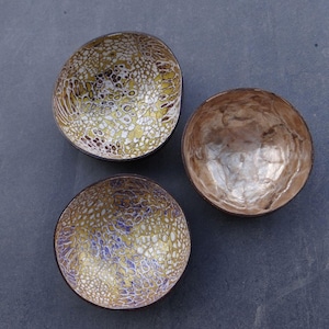May include: Three decorative bowls with intricate patterns. Two bowls feature a yellow, white, and purple design, while the third bowl has a metallic, brown interior. The bowls are arranged on a dark gray surface.
