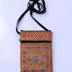 Puede incluir: Un peque&ntilde;o bolso bandolera rectangular bordado con una correa negra. El bolso presenta un colorido patr&oacute;n geom&eacute;trico en rojo, azul y dorado. Una cremallera negra recorre la parte superior. Es probable que el bolso est&eacute; hecho a mano.