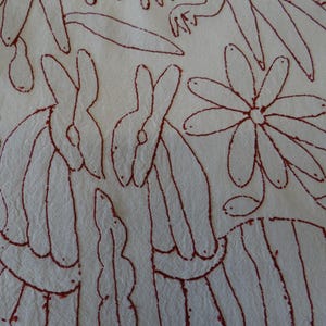 K&ouml;nnte beinhalten: Cremefarbener Stoff mit einem sich wiederholenden Muster aus roten Umrissen. Das Design umfasst stilisierte Kaninchen, Blumen und Bl&auml;tter. Das Kunstwerk hat einen Volkskunststil.