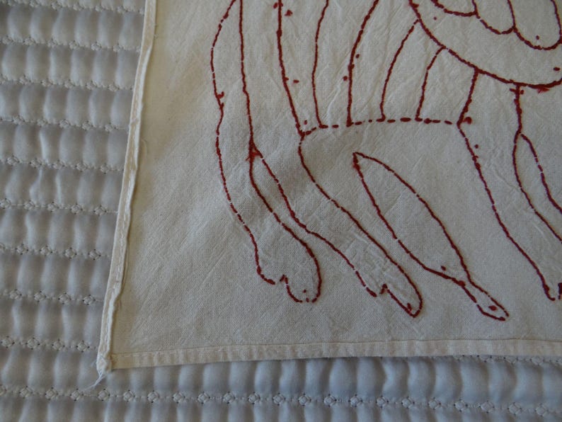 K&ouml;nnte beinhalten: Nahaufnahme eines wei&szlig;en Textils mit einem roten, abstrakten Design. Das Design scheint handgen&auml;ht oder gestickt zu sein. Das Textil liegt auf einer wei&szlig;en, gesteppten Oberfl&auml;che.