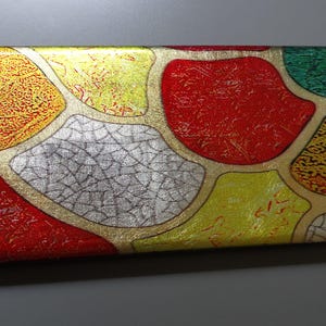 May include: Rectangular decorative box with a colorful abstract design. The box features a gold border and a pattern of red, yellow, silver, and green shapes. The design has a textured appearance.