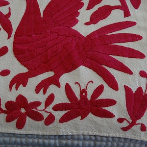 May include: Embroidered textile with a red rooster, flowers, and a butterfly on an off-white background. The detailed embroidery creates a textured surface, showcasing a folk art style. The design is likely part of a larger piece.