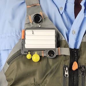 May include: A grey and orange fly fishing vest with a fly fishing tool attached to the front. The tool has a white foam pad and two yellow bobbers.