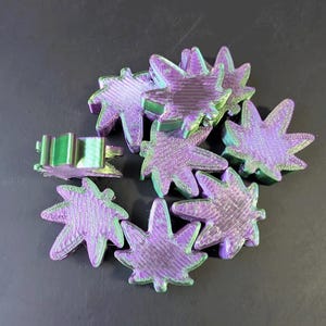 May include: A collection of purple and green leaf-shaped objects. The objects have a metallic sheen and are arranged in a circular pattern. The leaves have a textured surface and a gradient of colors.
