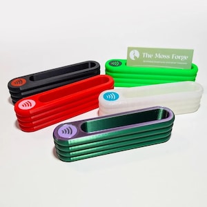 May include: A collection of colorful, rectangular card holders in black, red, green, white, and green-purple. Each holder has a rounded top with a wireless symbol and a slot for cards. A business card with the text "The Moss Forge" is in one.