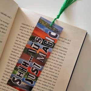 May include: A bookmark with the text "SHHH... IT'S JUST MAGIC" in a collage style. The bookmark has a green tassel and is placed in an open book. The bookmark's design features a mix of colors.