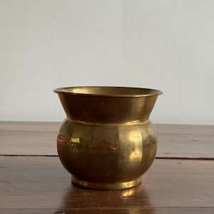 Peut inclure: Un petit bol en laiton poli avec un corps arrondi et bombé ainsi qu'un large bord évasé. La surface métallique présente une finition dorée chaleureuse avec des reflets subtils et une silhouette courbe lisse qui se rétrécit vers la base.