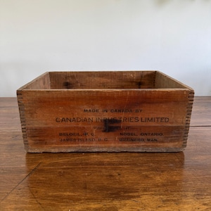 Könnte beinhalten: Eine rechteckige Holzkiste mit sichtbarer Holzmaserung. Die Kiste trägt den Text "MADE IN CANADA BY CANADIAN INDUSTRIES LIMITED" und andere Texte. Die Kiste steht auf einer Holzoberfläche.