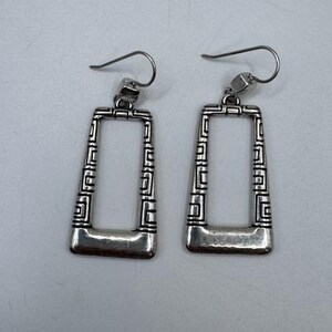May include: A pair of silver-toned rectangular earrings. Each earring features a geometric design along the edges and a curved bottom. The earrings have a hook closure for pierced ears.