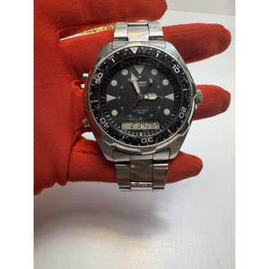 May include: A silver-toned Casio Quartz watch with a black face and digital display showing "2:3426". The watch has a rotating bezel with markings and a stainless steel band. The watch is water resistant to 100M.