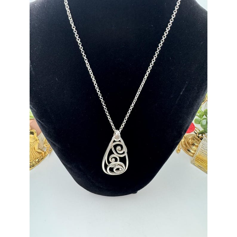 May include: Silver-toned pendant necklace with a teardrop-shaped pendant. The pendant features an openwork design with swirling patterns. The necklace chain is a delicate cable chain. The pendant is approximately 1.5 inches long.
