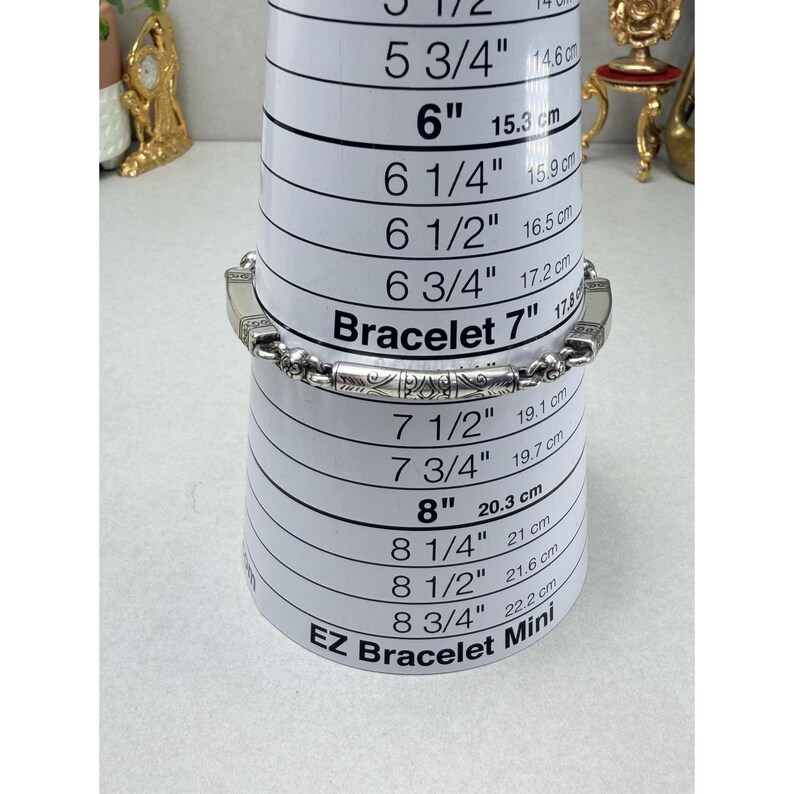 K&ouml;nnte beinhalten: Ein silbernes Armband mit einem verzierten Design wird auf einem Armband-Gr&ouml;&szlig;enwerkzeug angezeigt. Das Werkzeug zeigt Messungen in Zoll und Zentimetern an. Das Armband ist etwa 7 Zoll (17,8 cm) lang.