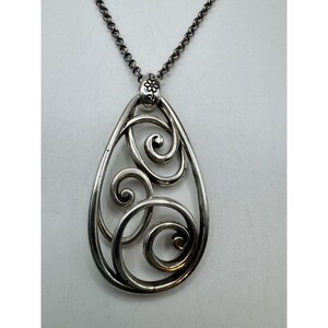 May include: Silver-toned pendant necklace featuring a teardrop-shaped openwork design with swirling scroll details. The pendant hangs from a delicate chain. The necklace has a floral accent at the top.