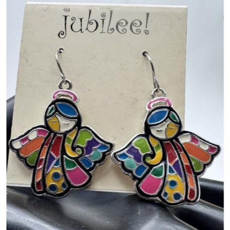 May include: A pair of silver-toned dangle earrings featuring colorful angel designs. Each angel has a blue head, a pink halo, and wings in shades of orange, green, purple, and pink. The earrings are displayed on a card that reads "jubilee!"