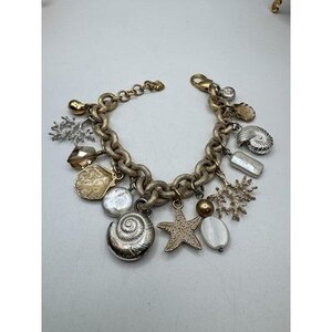 May include: A gold-toned charm bracelet featuring various sea-themed charms. The bracelet includes charms shaped like seashells, starfish, and coral, along with pearl and crystal accents. The chain is a chunky link design with a lobster clasp.