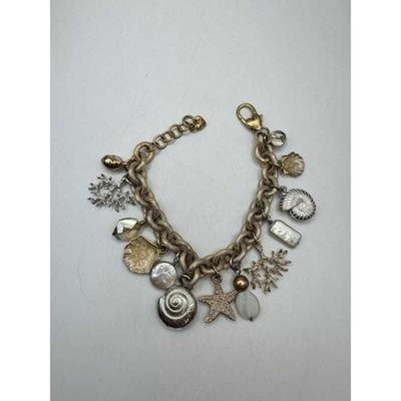 May include: A gold-toned charm bracelet featuring various ocean-themed charms. Charms include seashells, starfish, coral, and pearls. The bracelet has a lobster clasp closure and a chunky chain design.