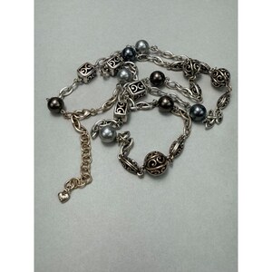 Może przedstawiać: Srebrny naszyjnik z mieszanką ciemnoszarych i srebrnych koralik&oacute;w, a także dekoracyjnych kwadratowych i okrągłych element&oacute;w filigranowych. Naszyjnik posiada łańcuszek z regulowaną długością.