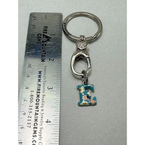 Peut inclure: Porte-cl&eacute;s argent&eacute; avec un charm en forme de lettre "E" bleu peint de motifs floraux. Le porte-cl&eacute;s comporte un c&oelig;ur orn&eacute; de pierres claires et un grand anneau. Le porte-cl&eacute;s mesure environ 7.6 cm de long.