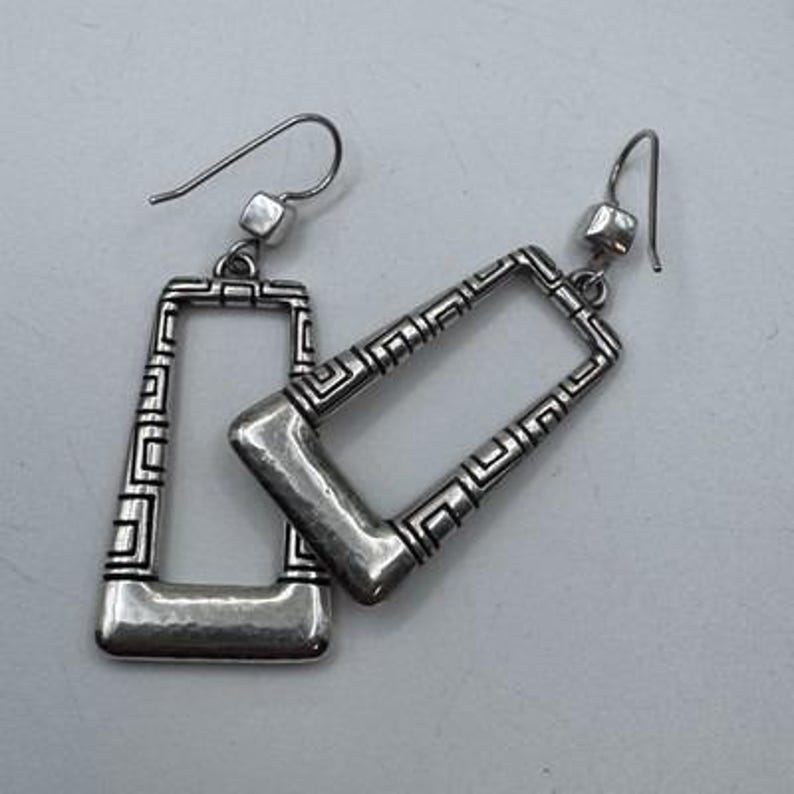 May include: A pair of silver-toned rectangular earrings. The earrings have a geometric design with a hammered finish on the bottom. The earrings have a hook closure.