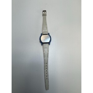 May include: A digital wristwatch with a blue face and a light gray band. The watch has a rectangular face with a silver-colored back. The band is made of a flexible material and has several holes for adjustment.