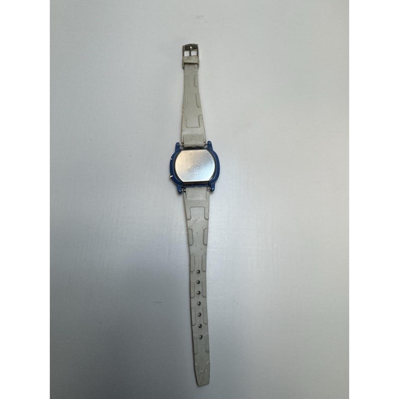 May include: A digital wristwatch with a blue face and a light gray band. The watch has a rectangular face with a silver-colored back. The band is made of a flexible material and has several holes for adjustment.