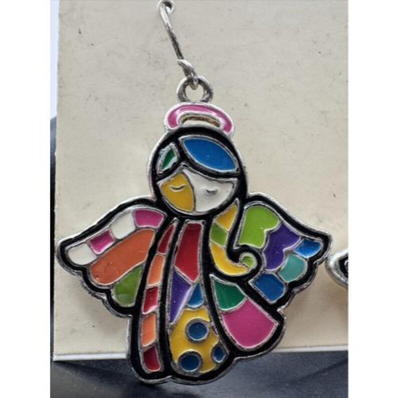 May include: A colorful angel earring with a silver-tone hook. The angel has a black outline and is filled with various colors, including red, yellow, blue, green, and pink. The angel has a halo and wings.