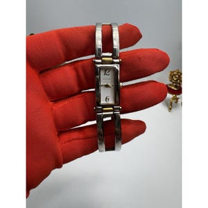 May include: A rectangular Bulova wristwatch with a silver-tone band and face. The watch has gold-tone accents and displays the numbers 12 and 6. The watch is a classic accessory.