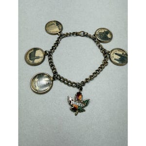 May include: Vintage silver-tone charm bracelet featuring round charms with black and white images of Quebec landmarks. A maple leaf charm with the word "Quebec" in colorful enamel hangs from the chain.