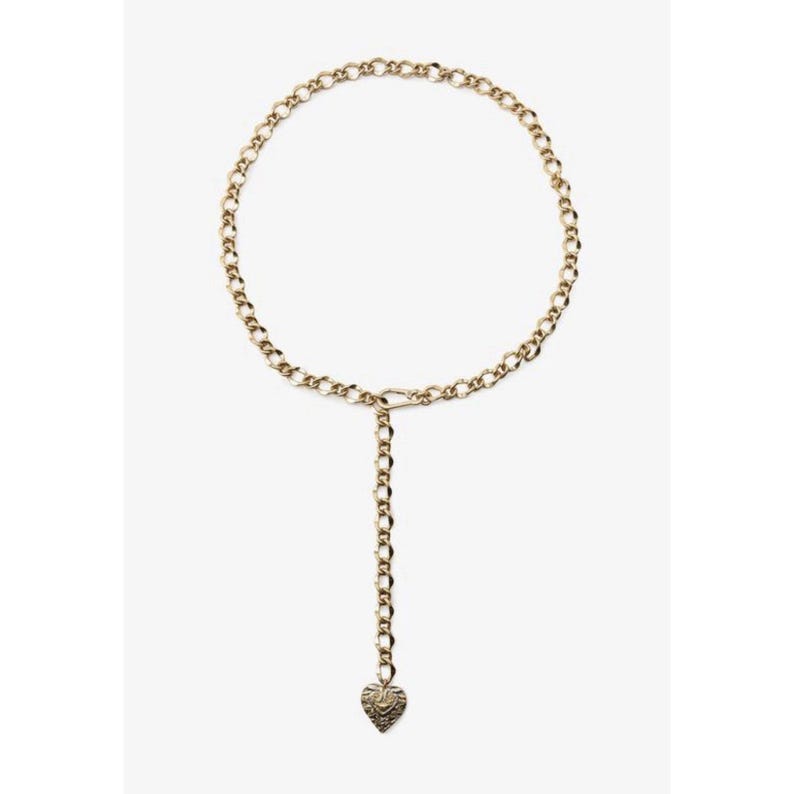 Puede incluir: Cintur&oacute;n de cadena dorado con colgante de coraz&oacute;n. El cintur&oacute;n presenta un dise&ntilde;o de cadena circular con una cadena colgante y un colgante en forma de coraz&oacute;n en el extremo. El colgante de coraz&oacute;n tiene una superficie texturizada.