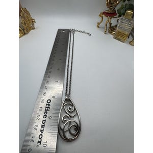 May include: Silver-toned pendant necklace with an open teardrop design featuring swirling patterns. The necklace is approximately 3 inches long, measured with a ruler. The chain is a dark silver color.