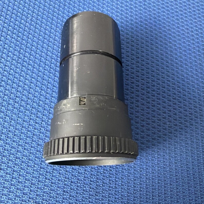 May include: A black cylindrical object with a ridged base and a smooth, glossy upper section. The object appears to be made of plastic or metal and is set against a blue textured background. The object has a small, rectangular marking.