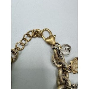 May include: Gold-toned charm bracelet with a heart-shaped clasp and various charms. The bracelet features a mix of chain styles and a silver-toned charm. The clasp is a gold heart shape.