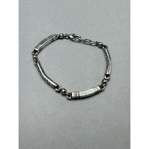 K&ouml;nnte beinhalten: Ein silbernes Armband mit rechteckigen und zylindrischen Gliedern. Die rechteckigen Glieder weisen ge&auml;tzte Muster auf, und das Armband ist durch kleine kugelf&ouml;rmige Glieder und eine Kette verbunden. Das Armband ist etwa 19 cm lang.