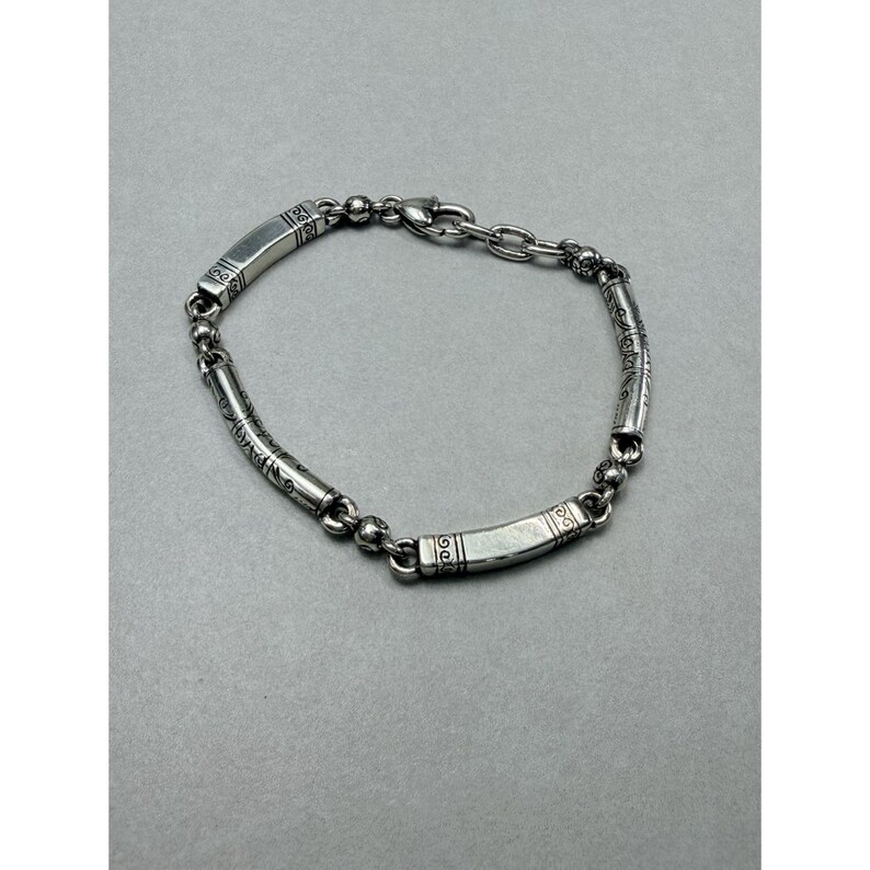 K&ouml;nnte beinhalten: Ein silbernes Armband mit rechteckigen und zylindrischen Gliedern. Die rechteckigen Glieder weisen ge&auml;tzte Muster auf, und das Armband ist durch kleine kugelf&ouml;rmige Glieder und eine Kette verbunden. Das Armband ist etwa 19 cm lang.