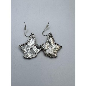 May include: A pair of silver-toned earrings. Each earring features a stylized, four-lobed floral design with a textured surface. The earrings have a hook closure for pierced ears.