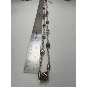 Może przedstawiać: Srebrny naszyjnik z r&oacute;żnymi koralikami i ogniwami łańcucha. Naszyjnik zawiera okrągłe, kwadratowe i wzorzyste koraliki. Linijka pokazuje, że naszyjnik ma około 18 cm długości.