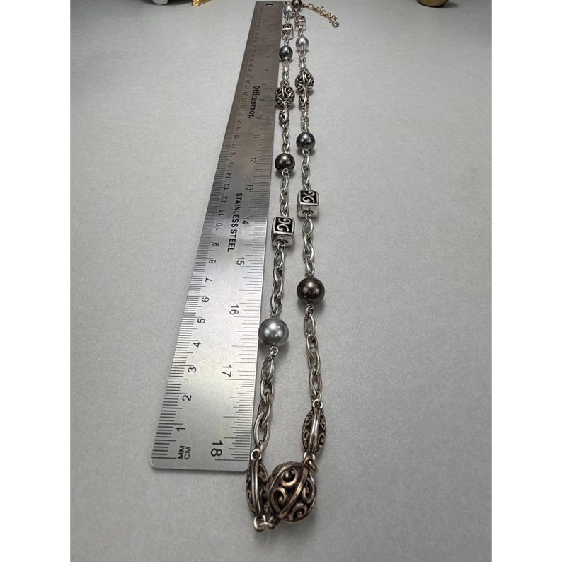 Może przedstawiać: Srebrny naszyjnik z r&oacute;żnymi koralikami i ogniwami łańcucha. Naszyjnik zawiera okrągłe, kwadratowe i wzorzyste koraliki. Linijka pokazuje, że naszyjnik ma około 18 cm długości.