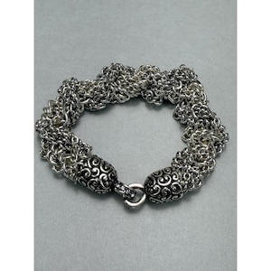 May include: Silver-toned bracelet featuring multiple strands of delicate chain links. The bracelet has decorative, patterned end caps and a secure clasp. The design is intricate and detailed, suitable for everyday wear or special occasions.