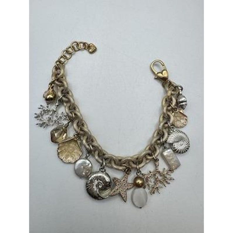 May include: A gold-toned charm bracelet featuring various ocean-themed charms. The bracelet includes charms shaped like seashells, starfish, and coral, along with a lobster clasp closure. The chain is a thick, textured design.