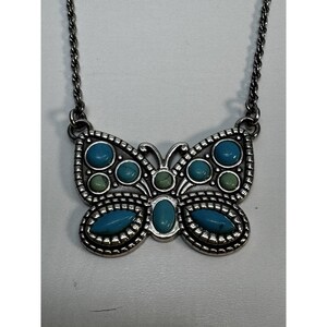 May include: Silver-tone butterfly pendant necklace with turquoise and green stone accents. The butterfly pendant has a detailed, textured design and is suspended from a delicate chain. A stylish accessory.