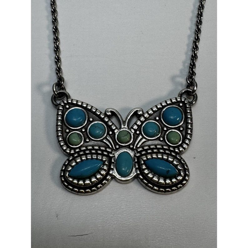 May include: Silver-tone butterfly pendant necklace with turquoise and green stone accents. The butterfly pendant has a detailed, textured design and is suspended from a delicate chain. A stylish accessory.