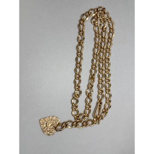 Puede incluir: Un cintur&oacute;n de cadena dorado con un colgante en forma de coraz&oacute;n. La cadena est&aacute; hecha de eslabones ovalados entrelazados. El colgante de coraz&oacute;n tiene una superficie texturizada con un dise&ntilde;o. El cintur&oacute;n tiene un cierre.