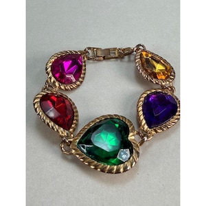 May include: A gold-tone metal link bracelet featuring five large, faceted, teardrop-shaped stones in vibrant colors including magenta, orange, red, purple, and a central heart-shaped green stone, all set within textured, rope-style metal frames.